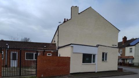 A white building pictured side-on, with a redbrick extension behind it.