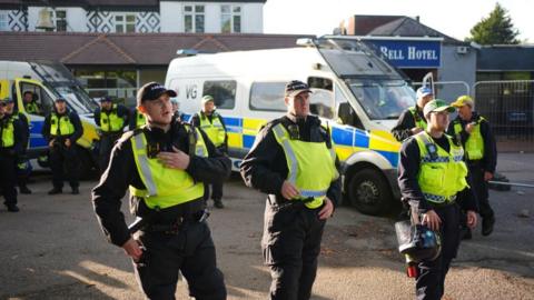 Police officers in uniform with vans behind them stand outside a hotel
