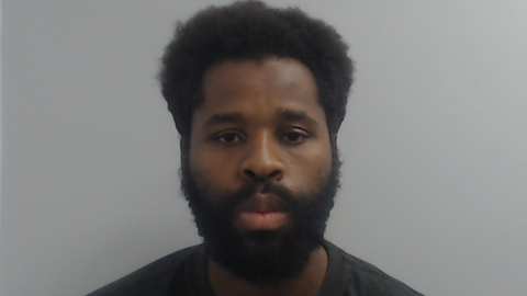 Police custody mugshot of Fabrice Kapena, who has a black beard and is wearing a black t-shirt.