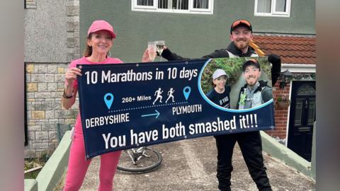 Sarah-Jane Hill standing with her son Taylor Hill in Plymouth, holding a banner after completing a 260-mile run from Somercotes.