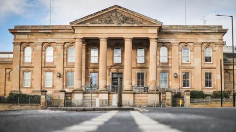 The High Court in Dundee, a brown brick building with pillars at the front, under a cloudy blue sky.