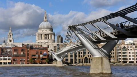 St Paul's Cathedral in the background, with the Millennium Bridge in the foreground. The photo is taken from river level, looking up at the bridge and cathedral, with the River Thames visible at the bottom.