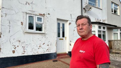 Simon Gibbons on the drive of his council-owned home in Budleigh Salterton with multiple patches and cracks in the rendering