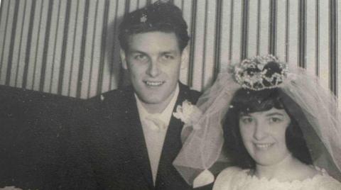 A man wearing a jacket and a woman wearing a white wedding dress sitting inside.
