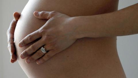 Close-up of a woman who has her hands around her pregnant stomach