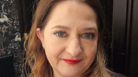 A close up of a woman, Nicola Lovell. She is white and has green eyes, she wears red lipstick
