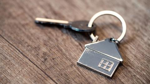 A house key and house-shaped key fob laid out on a wooden table