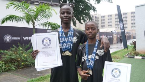 Brothers Victor and Confidence Kipo stand with medals around their necks and holding Guinness World Record certificates