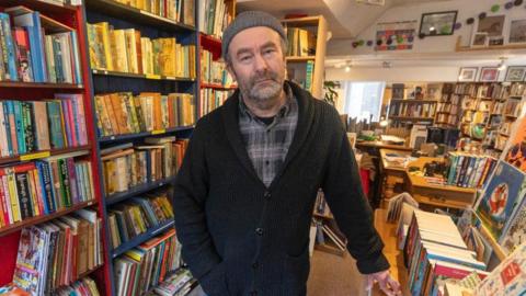 Bearded Paul Hamer with grey beanie hat, black and grey checked shirt, black cardigan.