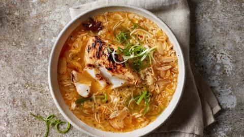 A bowl filled with rice in an orange broth, with flaky charred white fish on a mottled stone surface