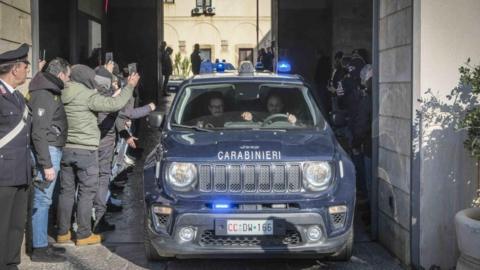 Police officers in Palermo drive through an entrance snapped by photographers