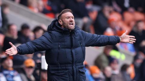 Blackpool boss Ian Evatt gesticulating with his arms out wide from his technical area, appealing against a decision which has gone against his side.