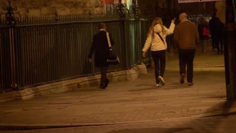 Three people walk through the street at night 