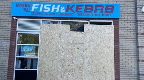 Shop with front window boarded up and sign saying "Moreton Hall Fish and Kebab"