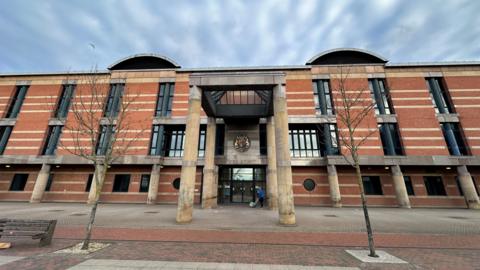 A large red brick court building with long dark windows and large columns supporting a porch.