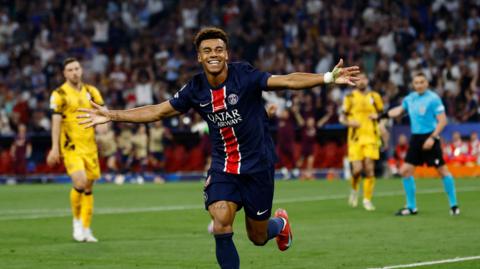 Desire Doue runs and holds his arms out in celebration of a goal