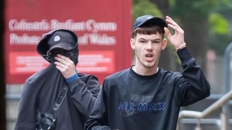 Jayden and Morgan walking outside of court, one in a baseball cap the other hiding his face in a hoodie