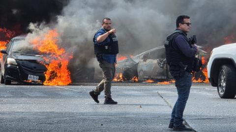 Police officers secure the area where cars were set on fire in a wave of violence following a military operation