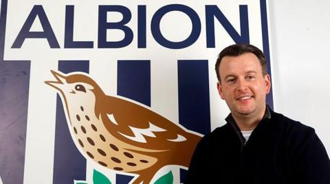 West Bromwich Albion technical director Dominic Price stands in front of a giant club crest