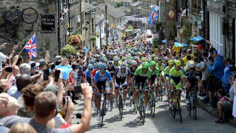 Crowds cheers on as cyclists peddle up a cobbled street