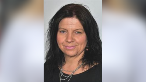 Michelle Vince smiles at the camera. She has shoulder-length dark hair and is wearing a black top and a silver multi-layered necklace.