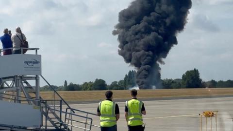 Four people look on as black smoke comes from the crashed plane in Southend