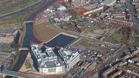 Aerial image of a range of buildings alongside the River Don, they sit within a drawn red boundary defining the Waterfront site