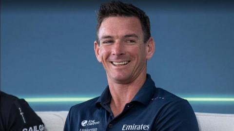 A man in a navy polo smiles looks off to the right of the camera.