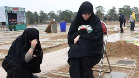 Two women crouch at the grave of a relative in a cemetary in Tehran on 16 March