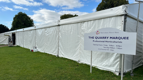 A white flower show marquee on the grass in Shrewsbury's Quarry park. A sign outside reads: The Quarry Marquee, with the opening hours for the 2024 event
