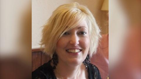 Kirsty Ireland looking at the camera smiling. She has blonde hair, a black top and large black dangling earrings.
