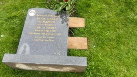 A headstone laid flat on planks of wood over the plot at a cemetery