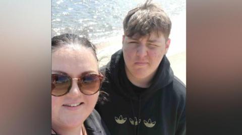 Marrissa Mullans has sunglasses, tied back brown hair and a black top. Her teenage Alfie is photographed with light brown hair and is wearing a black hoodie.