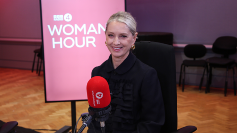 Katherine LaNasa has blonde hair pulled away from her face. She sits in front of a microphone and smiles at the camera.