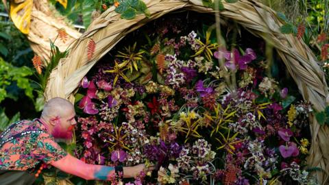 Man with pink facial hair tends to some flowers of the same hue.