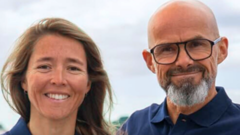 Two people - Audrey Ogereau and Erwan Leroux - smiling and standing side by side outdoors. The person on the left - Audrey - has long brown hair and the person on the right - Erwan - is wearing glasses and is balding and has a beard. They are both wearing matching dark blue collared shirts.
