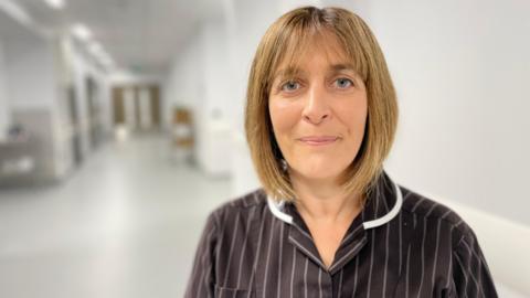 A nurse in dark stripped uniform stands in a hospital corridor