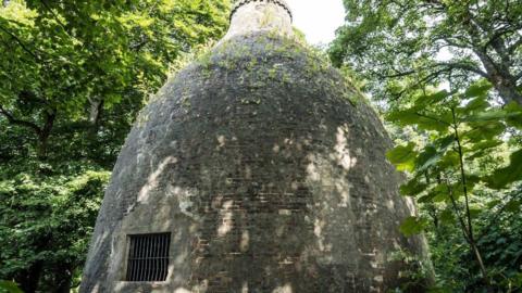 The bottle-shaped brick structure in Swinton is surrounded by woodland