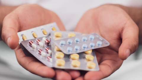 A hand holding a series of pharmaceutical drugs in packets.