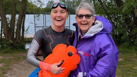 Dr Meg in her swimming attire, suit, cap and float, with her mother who is wearing a large purple overcoat.