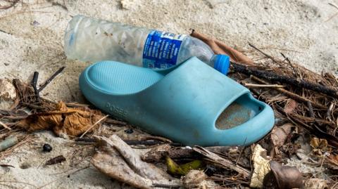 A blue slip-on sandal and a plastic water bottle on some sand