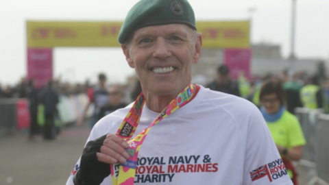 Chris Terrell having completed the Brighton Marathon, walking on crutches through the streets of the city. He is wearing a brightly coloured and logoed t-shirt and a green Royal Marines beret.