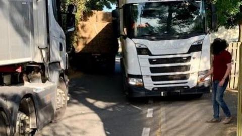 A lorry pulled to the side of a narrow road while an oncoming HGV is moving past