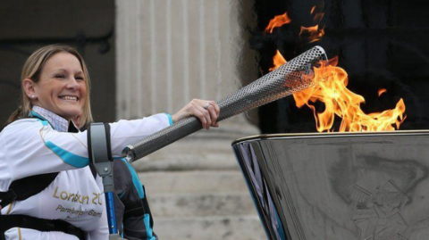 Claire Lomas holds a flaming torch over a steel cauldron