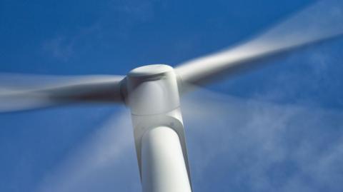 A wind turbine in close up with its blurred arms due to the speed of their movement against a blue sky