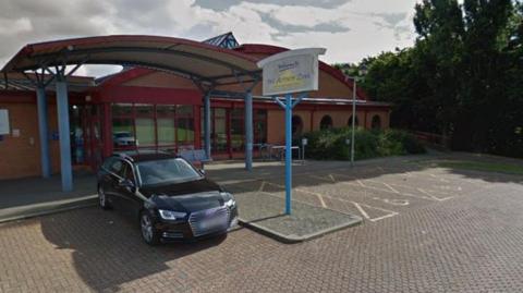 A sign outside of the Activity Zone leisure centre that says "activity zone". The building looks dated and there is a black car parked outside the entrance.