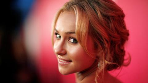Hayden Panettiere's head seen turned to look behind her and smile softly, in front of a red background