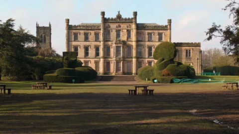 An exterior shot of Elvaston Castle with a wide green lawn, topiary bushes and picnic benches in front 