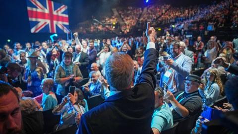 Nigel Farage is photographed from behind, as he gives a thumbs up in front of a large crowd and a big union flag in the National Exhibition Centre in Birmingham on 20 September