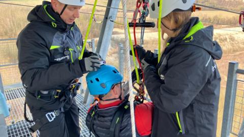 Lord Mackinlay of Richborough being fastened in on his zip wire